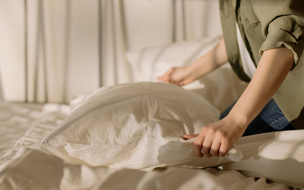 Person som bäddar sin säng med vita lakan, påslakan och kuddfodral.